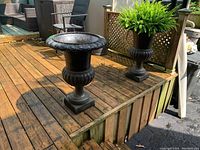 Front view of two black cast iron urn planters placed on outdoor wooden deck
