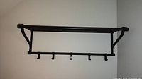 Full front view showing wall mounted metal coat rack with upper horizontal rod shelf and five hooks below.