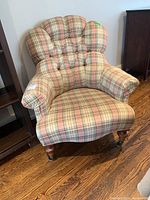 Front angle view of Ethan Allen plaid upholstered armchair with tufted back and wooden legs placed on a hardwood floor.
