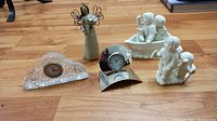 Photo of entire lot showing two clocks, metal angel ornament, and two Snow Babies style porcelain figurines on wooden floor.