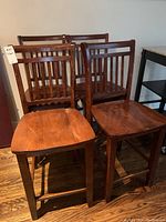 Four wooden high top chairs grouped together showing front and side views.