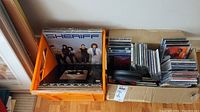 Photo showing a box containing assorted LP vinyl records including one with a cover featuring the band Sheriff, alongside a box of multiple CDs in cases.