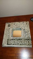 Mirror in square ceramic frame with Celtic knot pattern, detail of front showing raised relief design and aged texture.