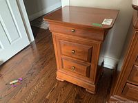 Front angled view of a wood night stand showing three drawers with metal knobs and the carved base.