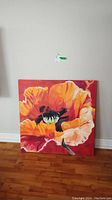 Full view of unframed acrylic painting of orange flower on canvas leaning against a wall.