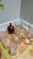 Lot arranged on the floor showing all glass items including pitchers, vases, cake plate, beer mug, and red decorative glass piece.
