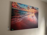 Photo of the large canvas print from an angle showing the beach sunset with waves and clouds reflecting on wet sand.