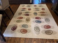 View of area rug laid flat on wooden floor, showing multicolor oval swirl patterns and overall rug size.