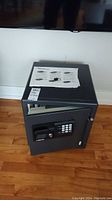 Front view of the Sentry Safe showing electronic keypad, key lock, instruction manual, and keys on top of safe.