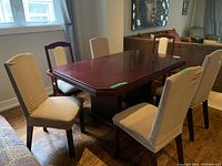 Six dining chairs around a wooden dining table, four without arms with beige slipcovers and two armchairs without slipcovers.