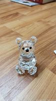 Clear Swarovski crystal bear figurine on wooden surface, showing full front and details such as black eyes and nose.