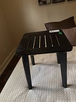 Black manufactured wood side table with four legs shown from an angle highlighting slatted top and overall shape.