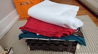 Stack of five folded fabric pieces including white textured pad, red cloth, teal cloth, patterned dark brown runner.