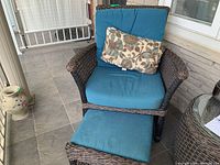 Front view of wicker lounge chair with cushion and footstool on tiled porch