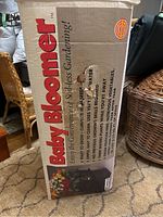 Tall rectangular cardboard box showing Baby Bloomer brand name and product description including hydroponic gardening features.