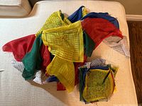 Two sets of Buddhist prayer flags in multiple colors with printed prayers and symbols, photographed together on a white cushioned surface.
