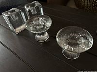 Four glass candleholders on a wooden table, two square block style and two pedestal style with floral patterns