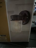 Photo showing Hampton Bay exterior wall light in black finish with visible glass shade and round mounting plate.