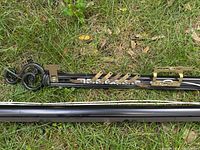 Two brown/black metal curtain rods laid on grass, showing multiple attached brass-colored curtain clips and curled decorative finials.