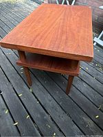 Photo of rectangular teak veneer side table showing top and tapered legs with brass capped feet on outdoor decking.