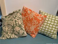 Three Mid-Century Modern style throw pillows arranged on a blue surface against a white wall, showing various fabric patterns and colors.