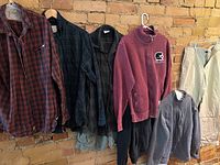 Full view of all clothing items hanging against exposed brick wall, showing variety of shirts, sweaters, pants, and shorts