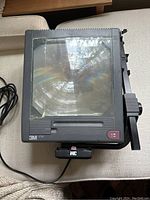 Top view of the overhead projector showing glass projection surface with tape residue and power cord attached.