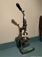 Front angled view of the heavy duty manual citrus juicer showing metal pressing cone, strainer and U-shaped base with black handle lifted.