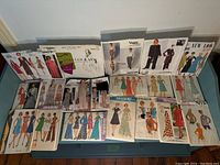 19 sewing pattern envelopes laid out on a surface, showing vintage dress and garment designs from multiple brands including New Look, Simplicity, Vogue, Style, Butterick, and Stitch N Sew.
