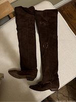 Overhead photo of both brown suede thigh high boots laid flat on cream chair showing full length and brown color.