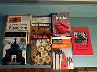 Photo of 8 books laid out on a blue surface showing titles related to travel, philosophy, and architecture.