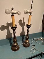 Pair of bronze and leather-wrapped table lamps without shades on a turquoise shelf, showing their turned column bases and white power cords coiled beside them.