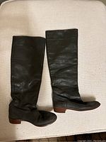 Pair of dark brown vintage leather knee-high boots laid flat, profile side view