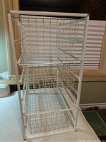 Front right angle view of the white wire shelf showing three wire basket drawers and white metal frame.