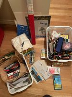 Overview of multiple baskets and paper bags containing mixed art supplies including sketch diary pad, markers, and packaged goods.