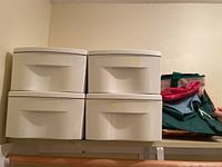 Four white plastic stacking bins arranged 2 by 2 on a shelf, showing front handles and top surfaces.