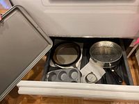 Photo showing large baking sheet held outside drawer containing other bakeware items.