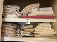 Folded queen size bed linens, blankets, and bed skirts on shelves in neutral tones