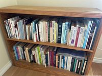 Photo showing two wooden bookshelf shelves filled with about 50+ assorted books, mainly on mental health, self help, and related topics.