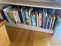 Books arranged on low shelf showing spines with titles like Joy of Cooking and The New York Times Cookbook along with various other titles