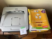 Brother HL-2140 laser printer with power cable and stacks of yellow Staples printer paper packs on side.