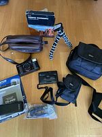 Full arrangement of all items including cameras, bags, tripod, digital recorder, strap, manual, and packaging placed on wooden floor.