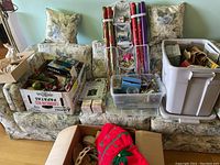 Photo showing floral couch with boxes and containers of Christmas ornaments, rolls of wrapping paper, and storage bins on and around it.