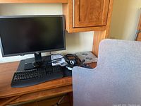 Acer 27-inch monitor, Microsoft ergonomic keyboard, Microsoft wired headset, laptop cooling tray with fans on wooden desk under wood desk hutch.