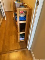 Side view of the wooden folding bookshelf placed in a hallway with visible three shelves containing various items.