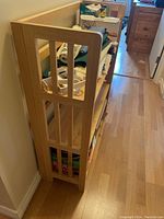 Side view of the wooden folding bookshelf showing vertical slats and three shelves with various household items.