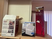 Three boxed items on wooden surface: Titan Rival Power Heater, Norelco air filter, and flex arm lamp.