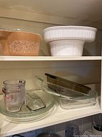 Overview of various Pyrex and Corning Ware bakeware including casseroles, mixing bowls, and glass baking dishes on shelves.