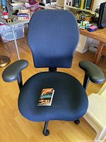 Blue fabric office chair from a frontal view showing seat, backrest, and adjustable arms.