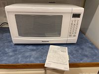 Front view of white Panasonic microwave on blue countertop with operating manual placed in front.